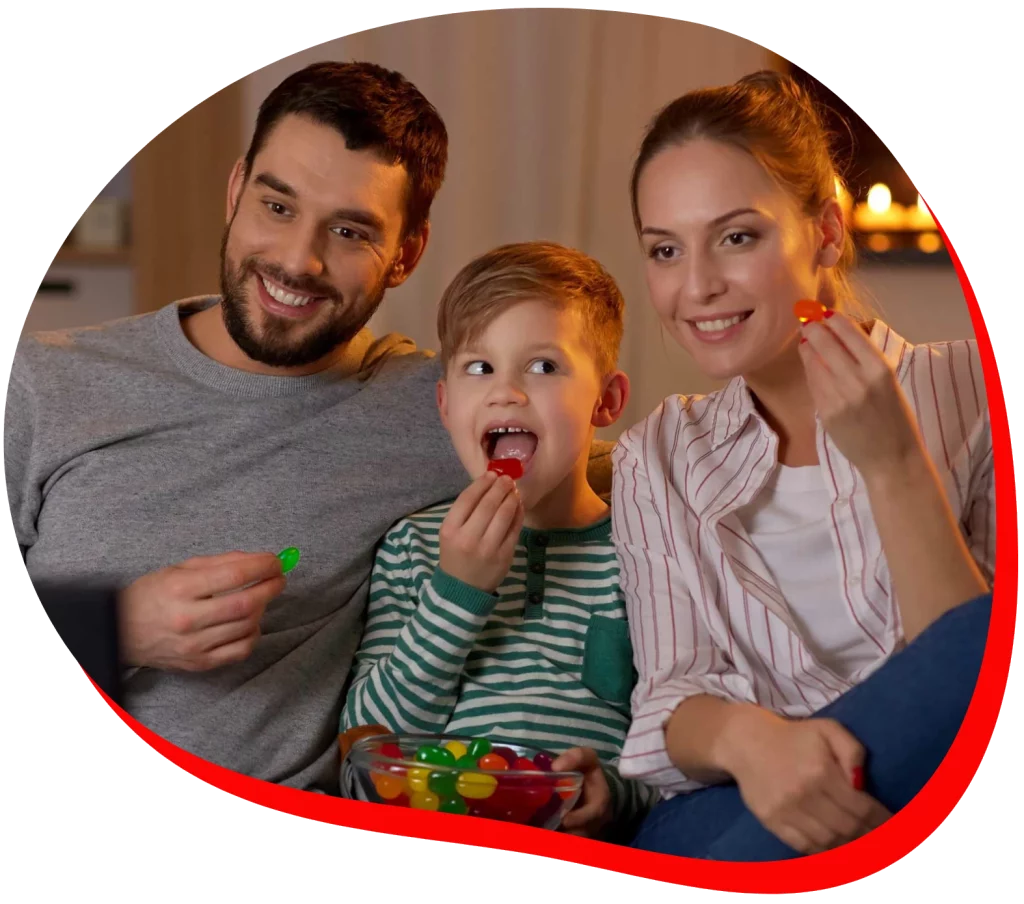 A family of three, sitting together on the sofa, enjoying jelly candies while watching TV.