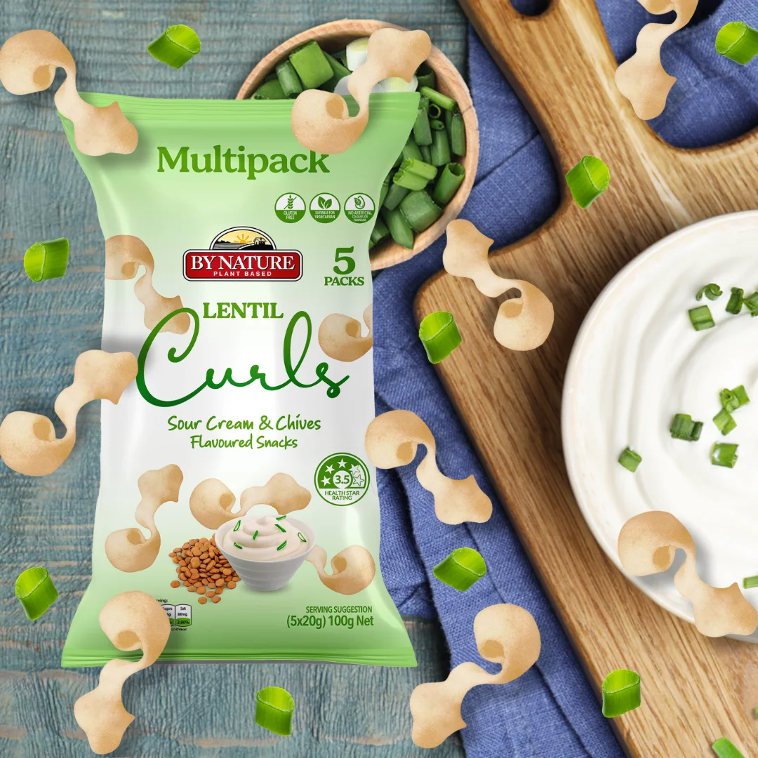 A packet of By Nature Lentil Curls Sour Cream & Chives flavoured snacks, surrounded by fresh chives and sour cream on a wooden background.