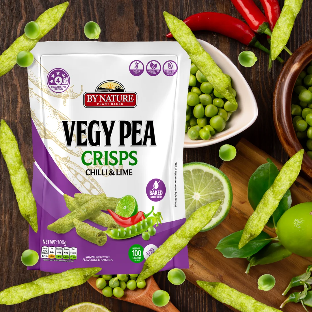 A packet of By Nature Vegy Pea Crisps in Chilli & Lime flavour, surrounded by fresh peas, lime slices, and red chillies on a dark wooden background.