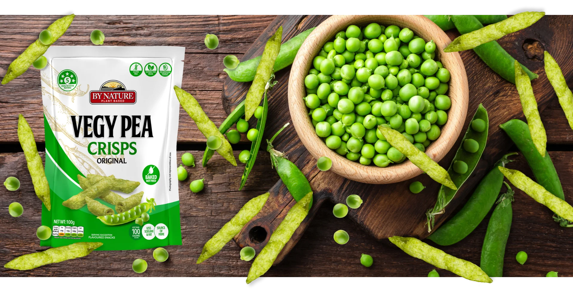 A stylised image of By Nature Vegy Pea Crisps Original packaging surrounded by green peas on a rustic wooden table.